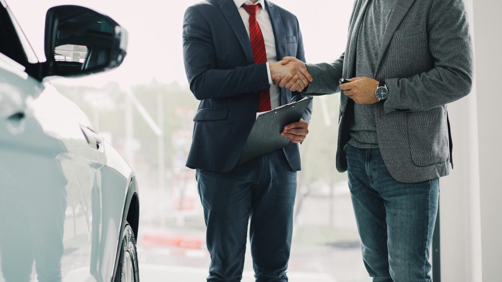 Two men shaking hands in a car dealership, symbolizing a successful business deal.